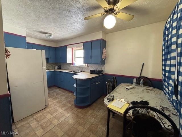 kitchen featuring white refrigerator, sink, blue cabinets, and ceiling fan