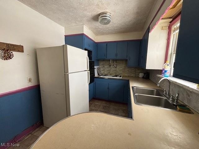 kitchen featuring blue cabinets, sink, tasteful backsplash, a textured ceiling, and white fridge