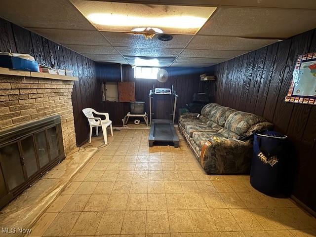 living room with a drop ceiling, a fireplace, and wood walls