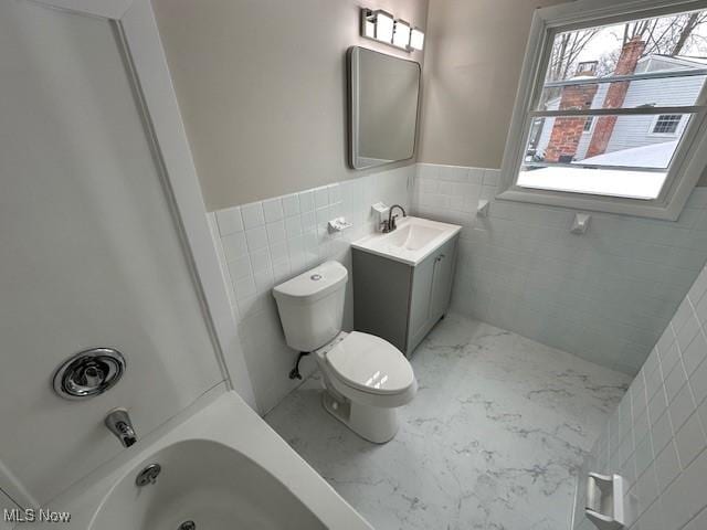 full bath with marble finish floors, plenty of natural light, tile walls, toilet, and a wainscoted wall