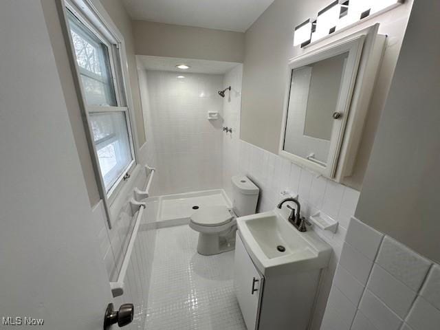bathroom featuring a tile shower, toilet, tile walls, vanity, and a wainscoted wall