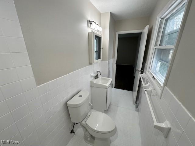 bathroom featuring tile walls, wainscoting, toilet, tile patterned flooring, and plenty of natural light