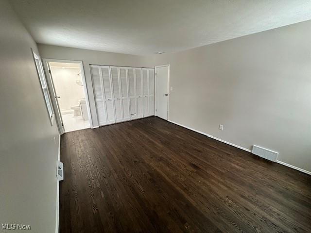 unfurnished bedroom featuring dark wood-style flooring, baseboards, a closet, and connected bathroom