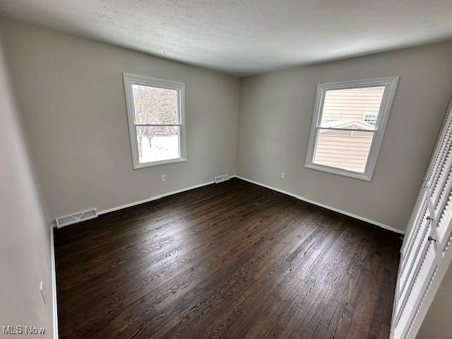 empty room featuring dark wood-style floors, plenty of natural light, and baseboards
