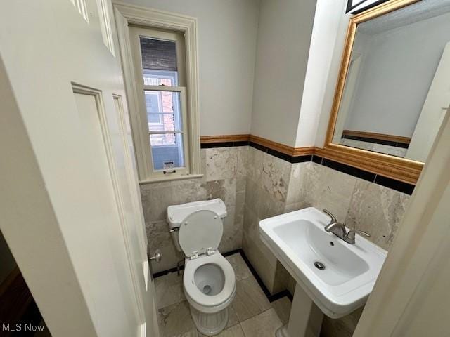 bathroom with tile patterned floors, toilet, sink, and tile walls