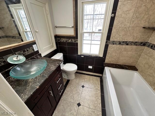 bathroom with tile patterned floors, toilet, tile walls, vanity, and a bathtub