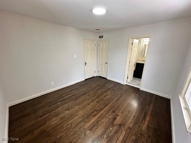 unfurnished bedroom featuring ensuite bath and dark wood-type flooring