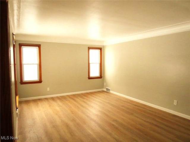 empty room with crown molding, plenty of natural light, and hardwood / wood-style floors