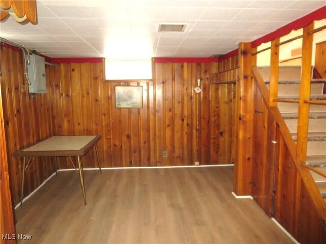 basement with wooden walls, electric panel, and hardwood / wood-style floors