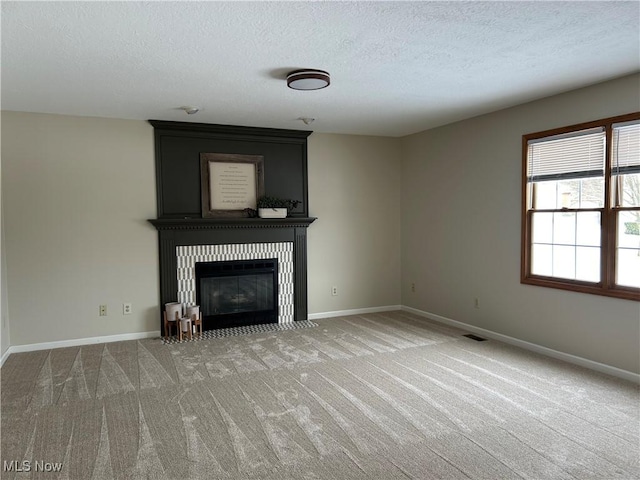 unfurnished living room with a tiled fireplace, carpet floors, and a textured ceiling