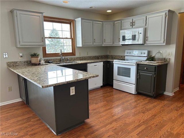 kitchen with dark hardwood / wood-style floors, sink, kitchen peninsula, light stone countertops, and white appliances