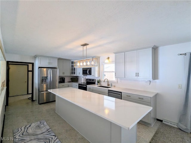 kitchen featuring sink, appliances with stainless steel finishes, a center island, a textured ceiling, and decorative light fixtures