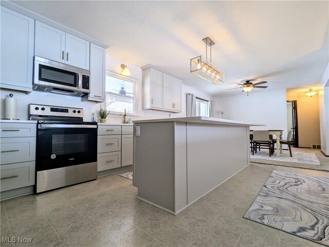 kitchen featuring ceiling fan, appliances with stainless steel finishes, a center island, white cabinets, and decorative light fixtures