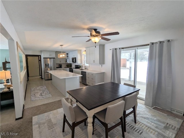 dining space featuring ceiling fan, sink, light colored carpet, and a textured ceiling