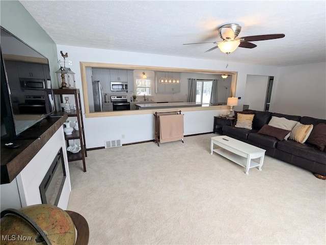 carpeted living room featuring ceiling fan, sink, and a textured ceiling