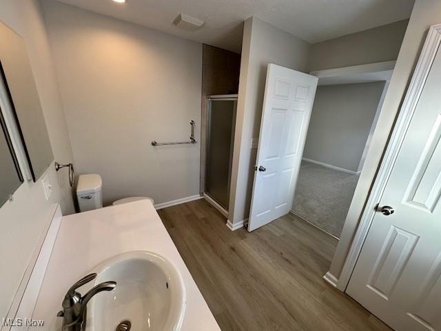 bathroom with a shower stall, wood finished floors, baseboards, toilet, and vanity