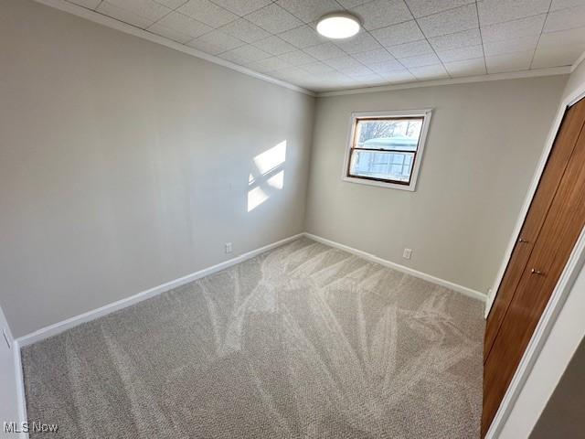 empty room featuring crown molding, carpet flooring, and baseboards