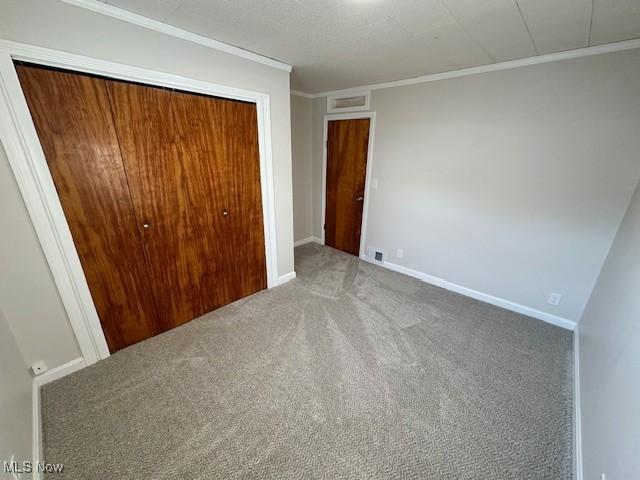 unfurnished bedroom with a closet, carpet, ornamental molding, and baseboards