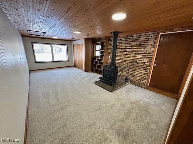 unfurnished living room featuring carpet flooring, a wood stove, brick wall, and wood ceiling