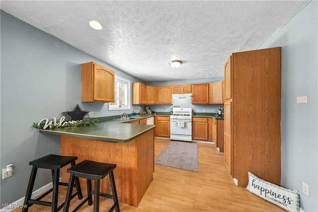 kitchen with light hardwood / wood-style floors, a textured ceiling, a kitchen bar, kitchen peninsula, and white gas stove