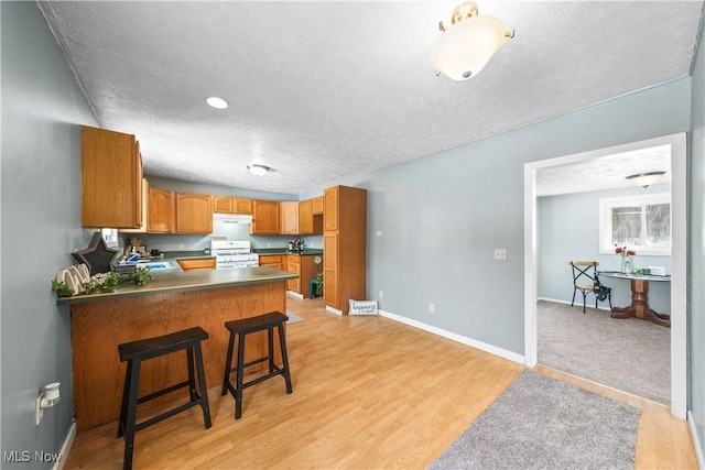 kitchen featuring a breakfast bar, light hardwood / wood-style flooring, a textured ceiling, white range with gas cooktop, and kitchen peninsula