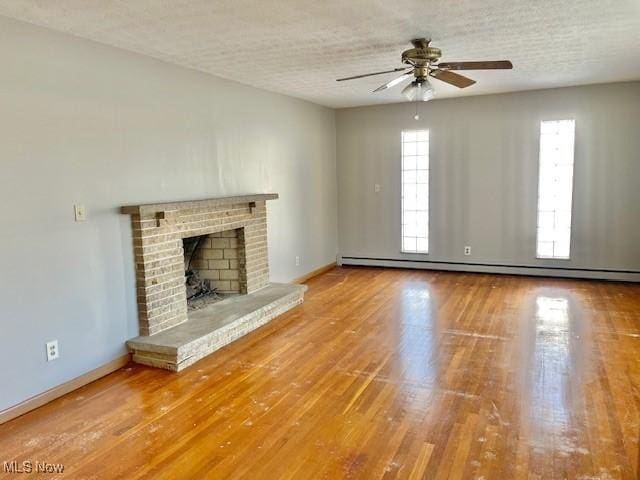 unfurnished living room featuring a baseboard heating unit, hardwood / wood-style flooring, a brick fireplace, and ceiling fan