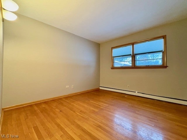 unfurnished room with baseboard heating and light hardwood / wood-style floors