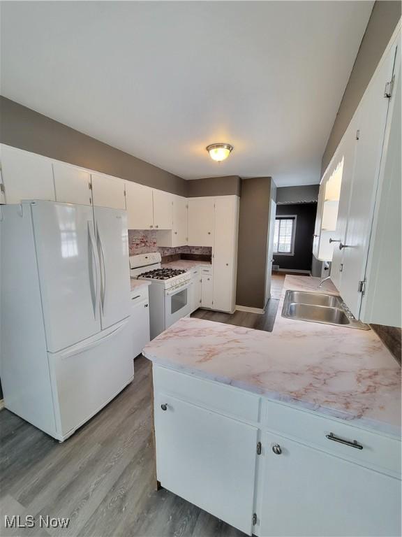 kitchen featuring tasteful backsplash, wood-type flooring, sink, white cabinets, and white appliances