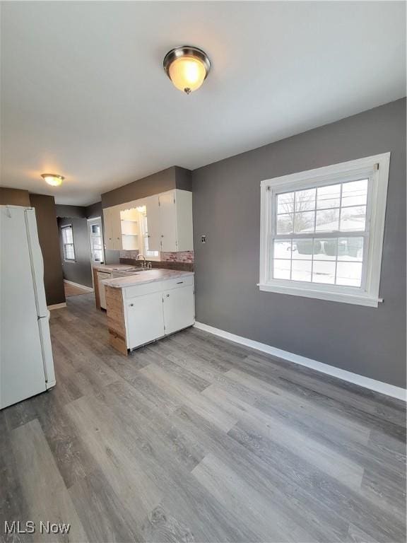 kitchen with white cabinetry, sink, white fridge, kitchen peninsula, and light hardwood / wood-style flooring