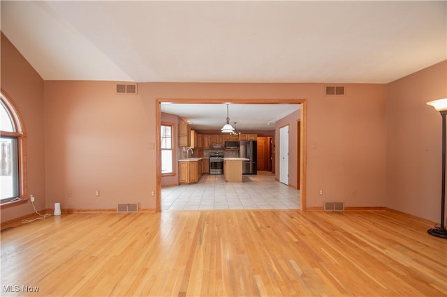 unfurnished living room with a healthy amount of sunlight, sink, and light hardwood / wood-style flooring