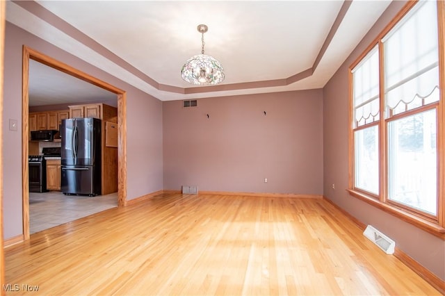 empty room with an inviting chandelier, light hardwood / wood-style flooring, and a raised ceiling