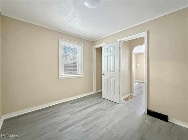 unfurnished bedroom featuring crown molding, a textured ceiling, and light wood-type flooring