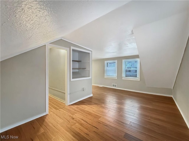 bonus room with built in features, lofted ceiling, hardwood / wood-style floors, and a textured ceiling