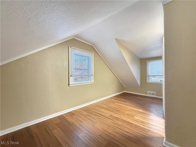 bonus room with lofted ceiling, wood-type flooring, and a textured ceiling