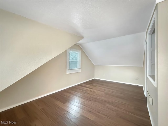 additional living space with vaulted ceiling, dark hardwood / wood-style floors, and a textured ceiling