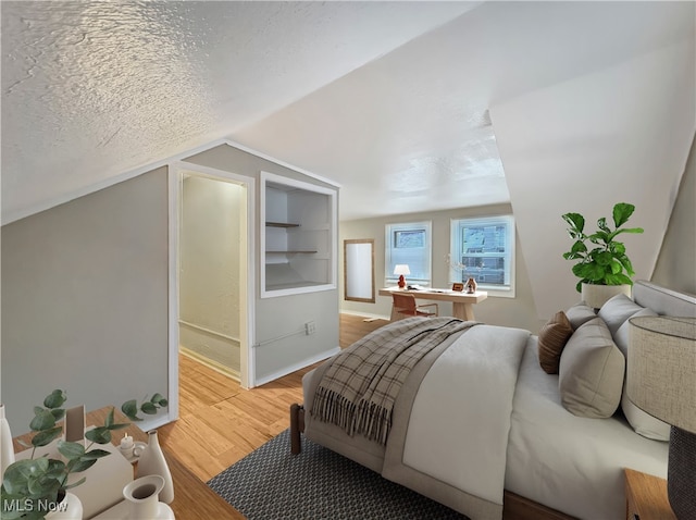 bedroom featuring lofted ceiling, hardwood / wood-style floors, and a textured ceiling