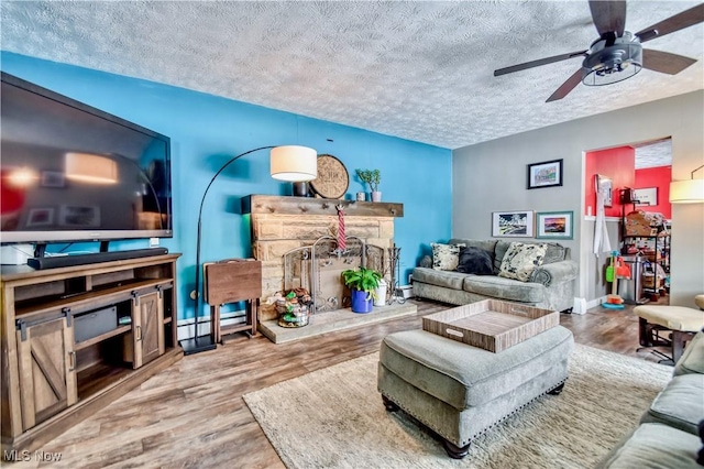 living room featuring ceiling fan, a stone fireplace, wood-type flooring, and a textured ceiling