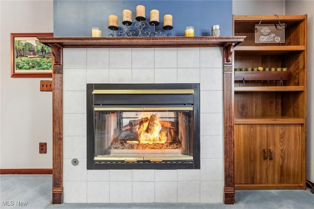 interior details with a tiled fireplace, carpet floors, and built in shelves