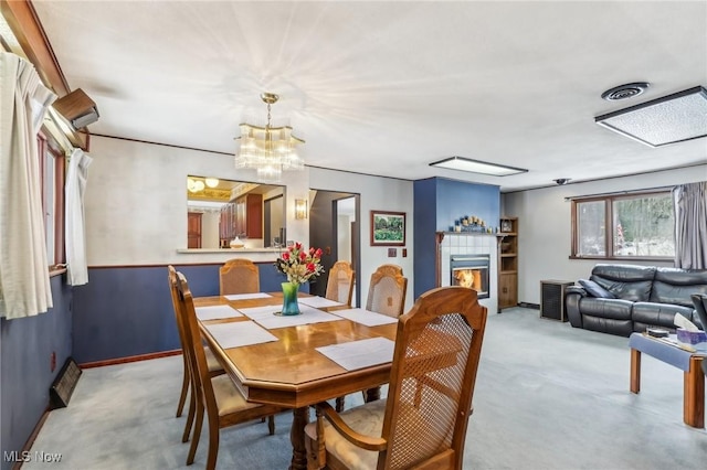 carpeted dining space featuring a tile fireplace and a notable chandelier