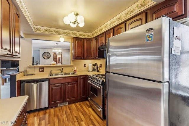 kitchen with sink, light hardwood / wood-style flooring, appliances with stainless steel finishes, hanging light fixtures, and a chandelier