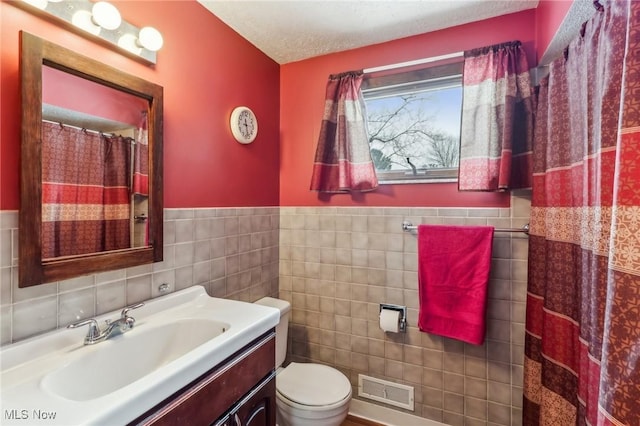 bathroom with tile walls, vanity, toilet, and a textured ceiling