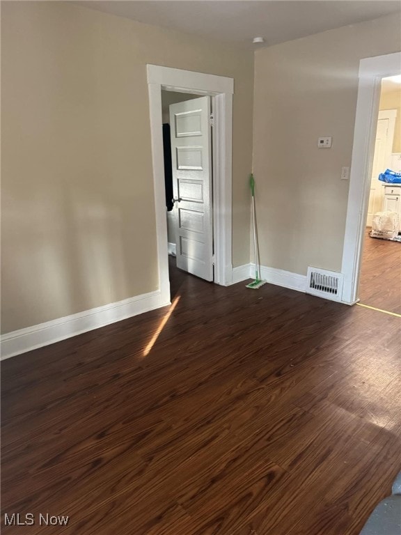 unfurnished room featuring dark wood-type flooring, visible vents, and baseboards