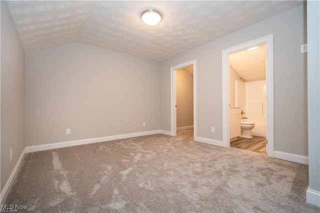 unfurnished bedroom featuring light colored carpet, connected bathroom, vaulted ceiling, a textured ceiling, and baseboards