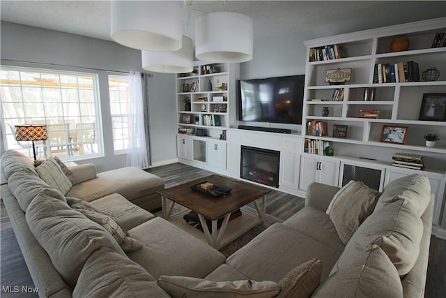 living area with dark wood-style floors, a glass covered fireplace, and built in features