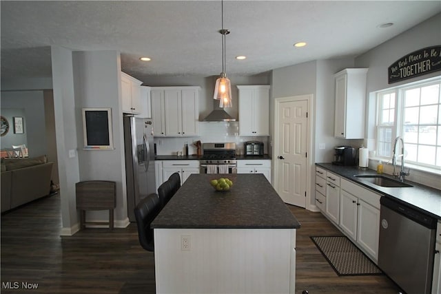 kitchen with wall chimney range hood, white cabinets, appliances with stainless steel finishes, and a sink