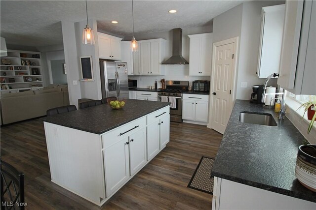 kitchen with dark countertops, wall chimney exhaust hood, appliances with stainless steel finishes, and a sink