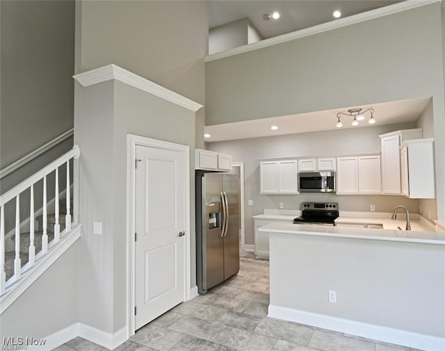 kitchen featuring sink, white cabinetry, appliances with stainless steel finishes, kitchen peninsula, and a towering ceiling