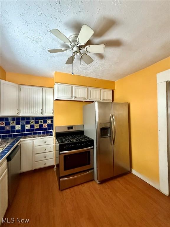 kitchen featuring white cabinetry, appliances with stainless steel finishes, tile counters, hardwood / wood-style flooring, and decorative backsplash