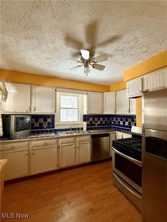 kitchen featuring sink, appliances with stainless steel finishes, ceiling fan, light hardwood / wood-style floors, and decorative backsplash