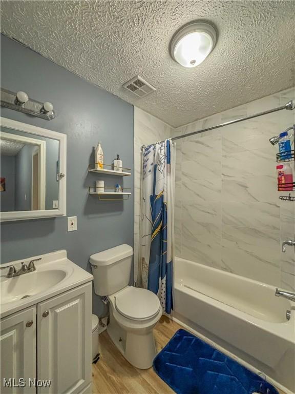 full bathroom with toilet, wood-type flooring, a textured ceiling, vanity, and shower / bathtub combination with curtain